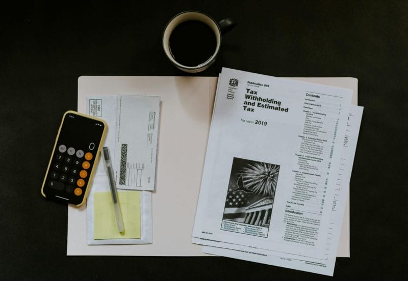 Desk with tax withholding paperwork, calculator, and coffee mug on black background