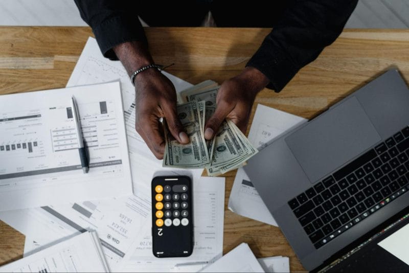 Person counting money with financial documents and calculator on desk